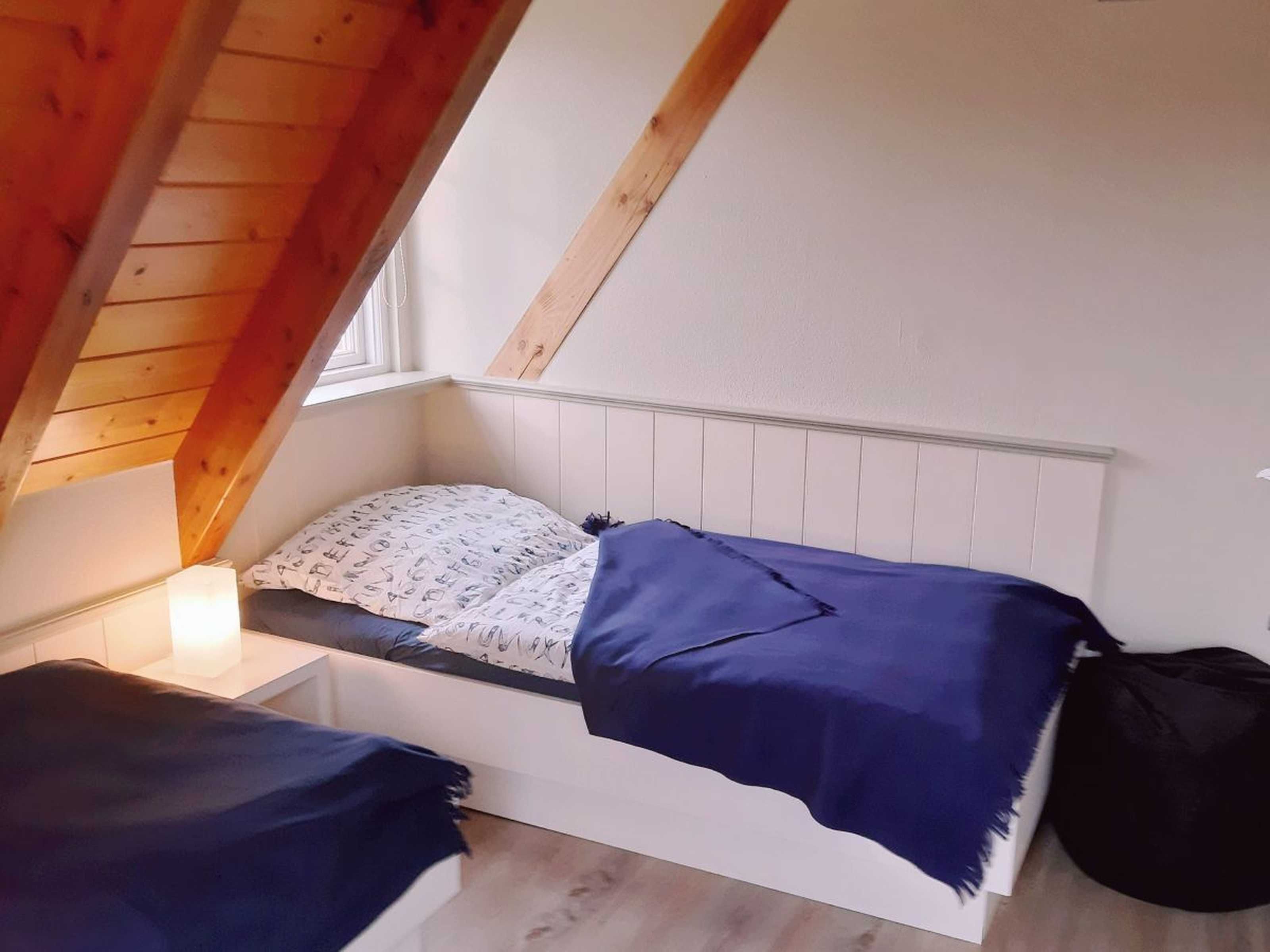 Un pequeño y acogedor dormitorio en el ático, con techo inclinado, una cama individual con un cojín estampado, una mesita de noche con lámpara y una ventana que proporciona luz natural.