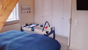 Quarto com uma cama de solteiro, um guarda-roupa branco, uma televisão e uma janela com persianas.