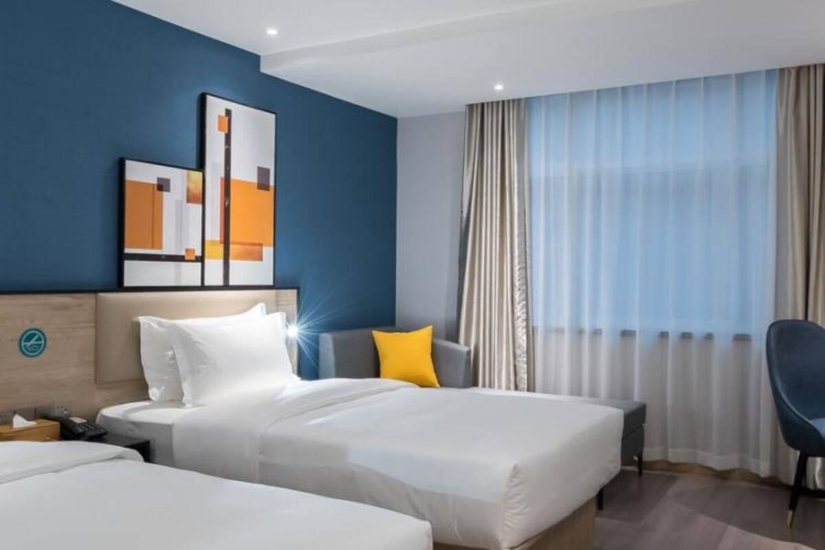 Ein Hotelzimmer mit zwei Betten, einem Schreibtisch, einem Stuhl und einem großen Fenster mit Vorhängen.