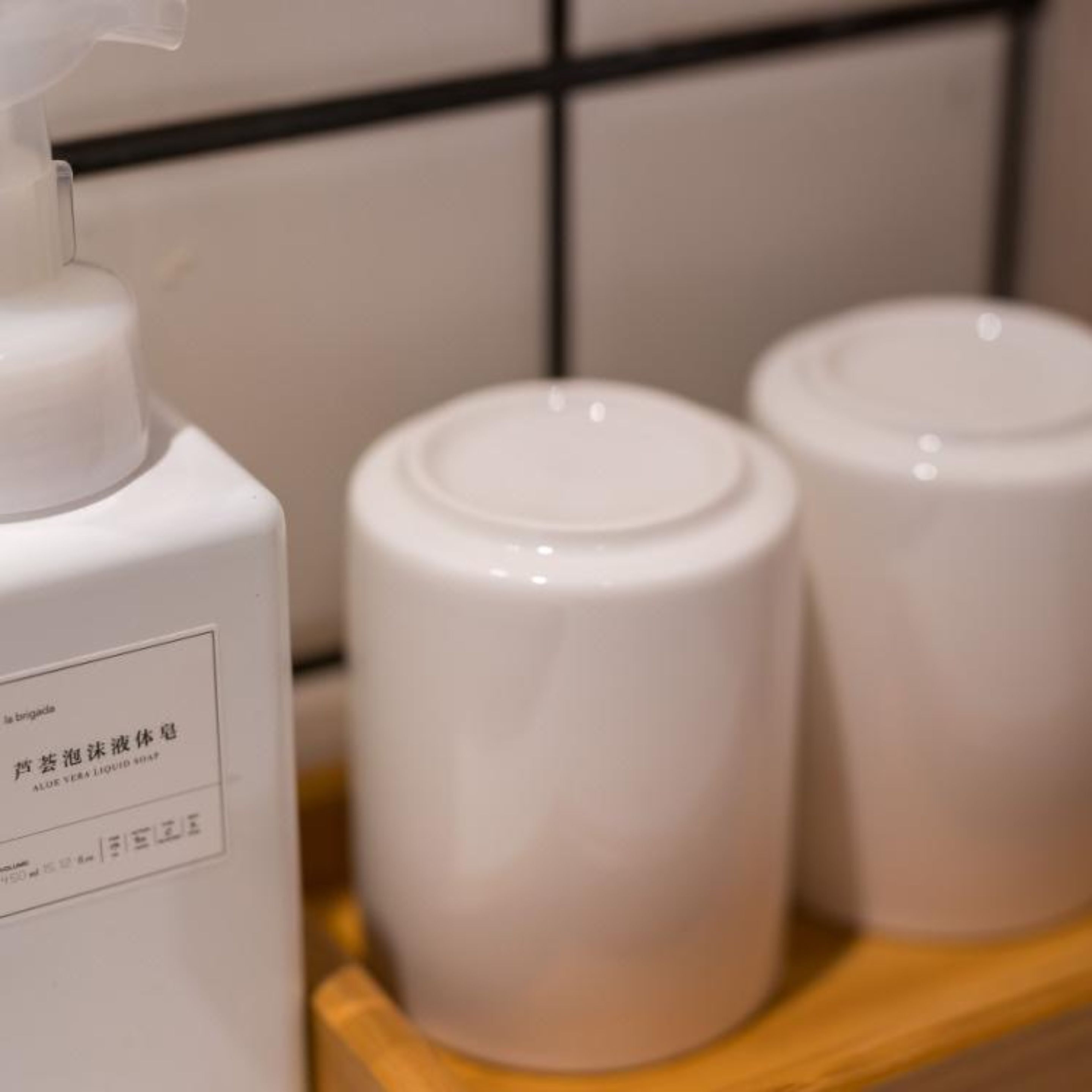 A bottle of liquid soap and two white containers on a wooden surface.