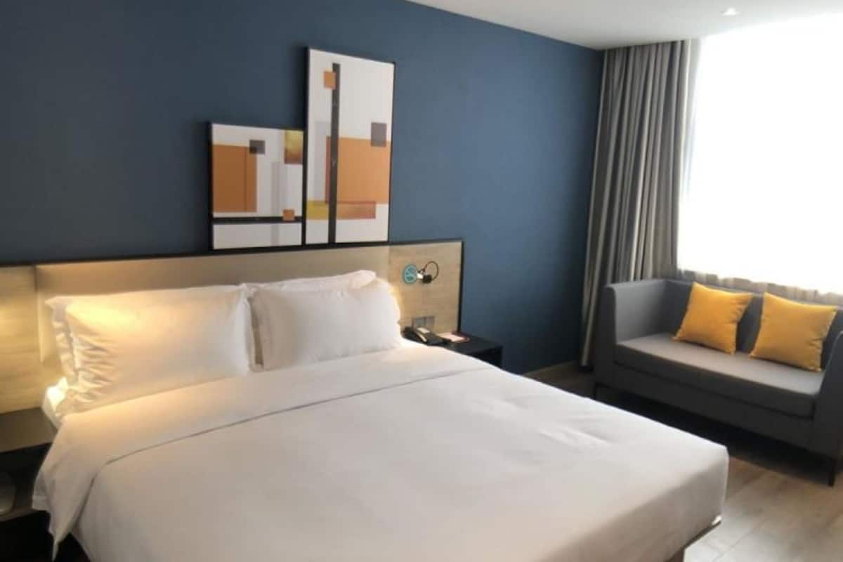 Ein Hotelzimmer mit einem großen Bett, einer Couch, einem Bild an der Wand und einem Fenster mit Vorhängen.