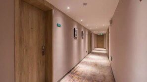 Corredor de hotel com portas de madeira, piso carpete e placa indicando a direção do elevador.