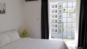 A modern hotel room with a large bed, a window with a view of a building, and an air conditioning unit on the wall. - Florence Apartment (Nha Trang)