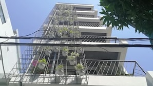A multi-story building with a balcony on the second floor, featuring a metal railing and potted plants. - Florence Apartment (Nha Trang)