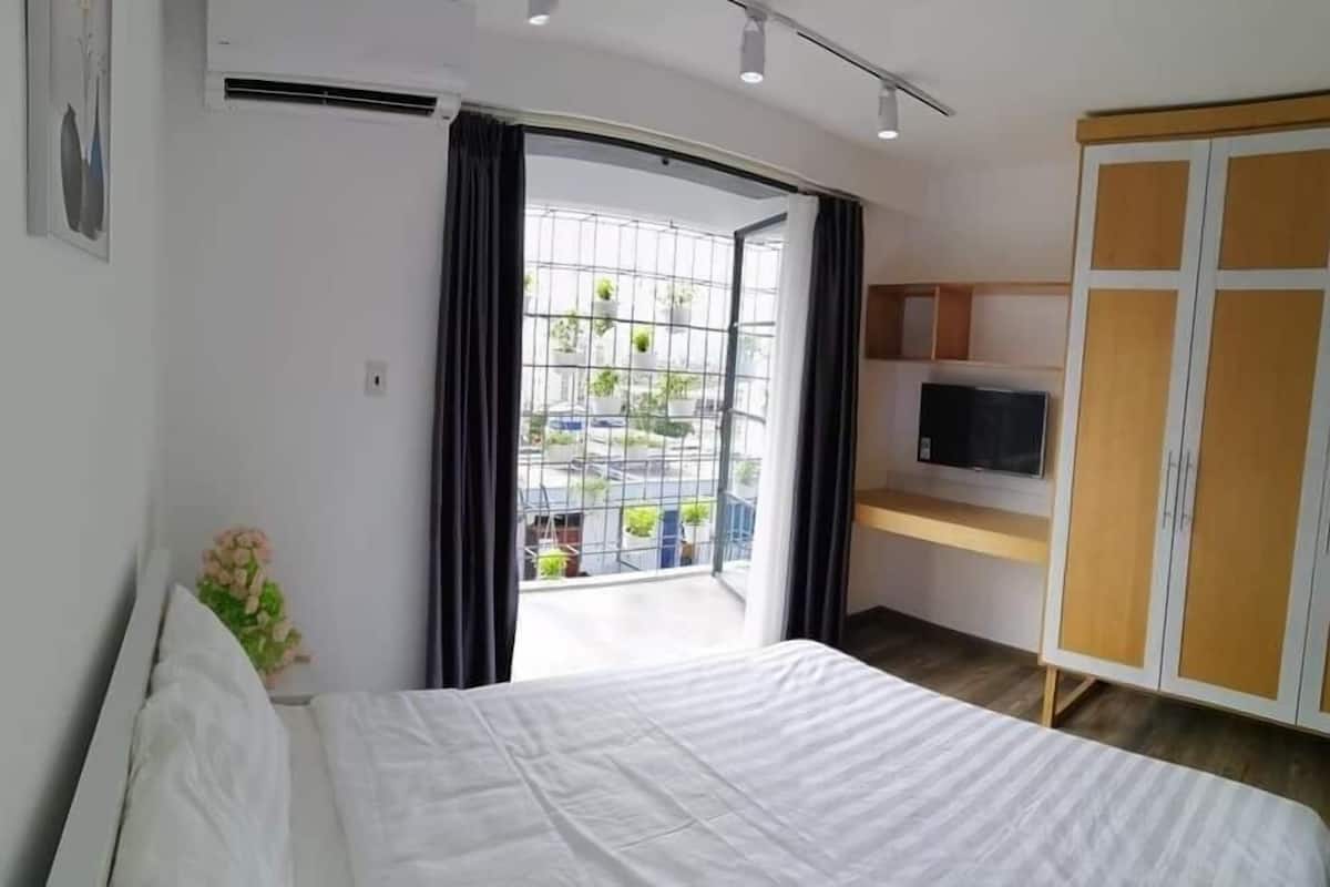 Ein Schlafzimmer mit Bett, Fernseher, Kleiderschrank und einem Balkon mit Topfpflanzen.