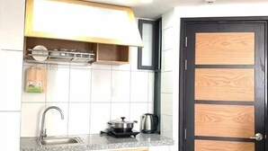 A compact kitchen with white tiled walls, a black door with wood paneling, and a countertop with a sink and stove. - Florence Apartment (Nha Trang)