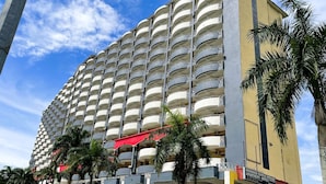 Un hotel de varios pisos con balcones, un letrero que indica que es un hotel y palmeras en la parte delantera.