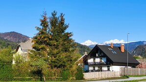Una casa con un recinto in legno, un albero grande e una catena montuosa sullo sfondo.
