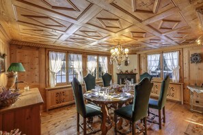 Une salle à manger aux murs lambrissés, avec une table ronde dressée pour six personnes, entourée de chaises recouvertes d’un tissu vert.