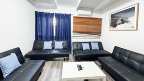 Een moderne woonkamer met twee zwarte leren banken, een witte salontafel en een groot raam met blauwe gordijnen.