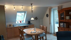 Uma cozinha com armários de madeira, uma mesa de jantar com cadeiras, uma cafeteira e uma estante de livros.