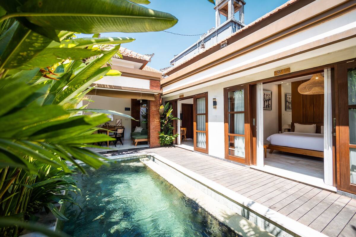 Ein Hotel mit Pool, einem Schlafzimmer mit Bett und Fenster sowie einem Essbereich mit Tisch und Stühlen.