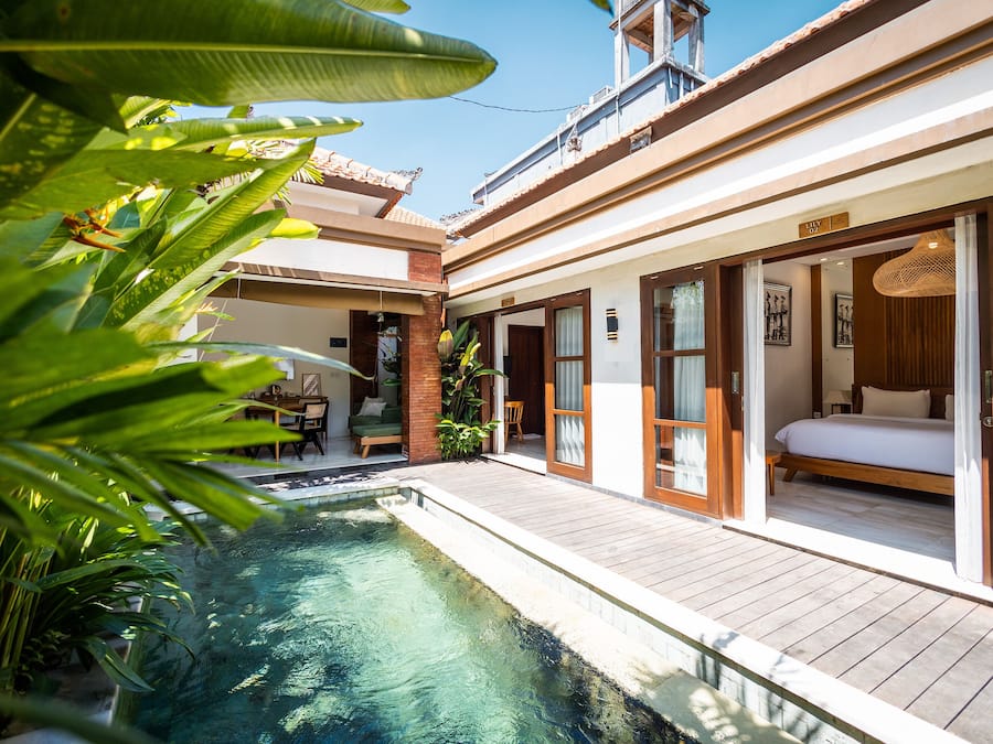 Hotel com piscina, quarto com cama e janela, e área de refeições com mesa e cadeiras.