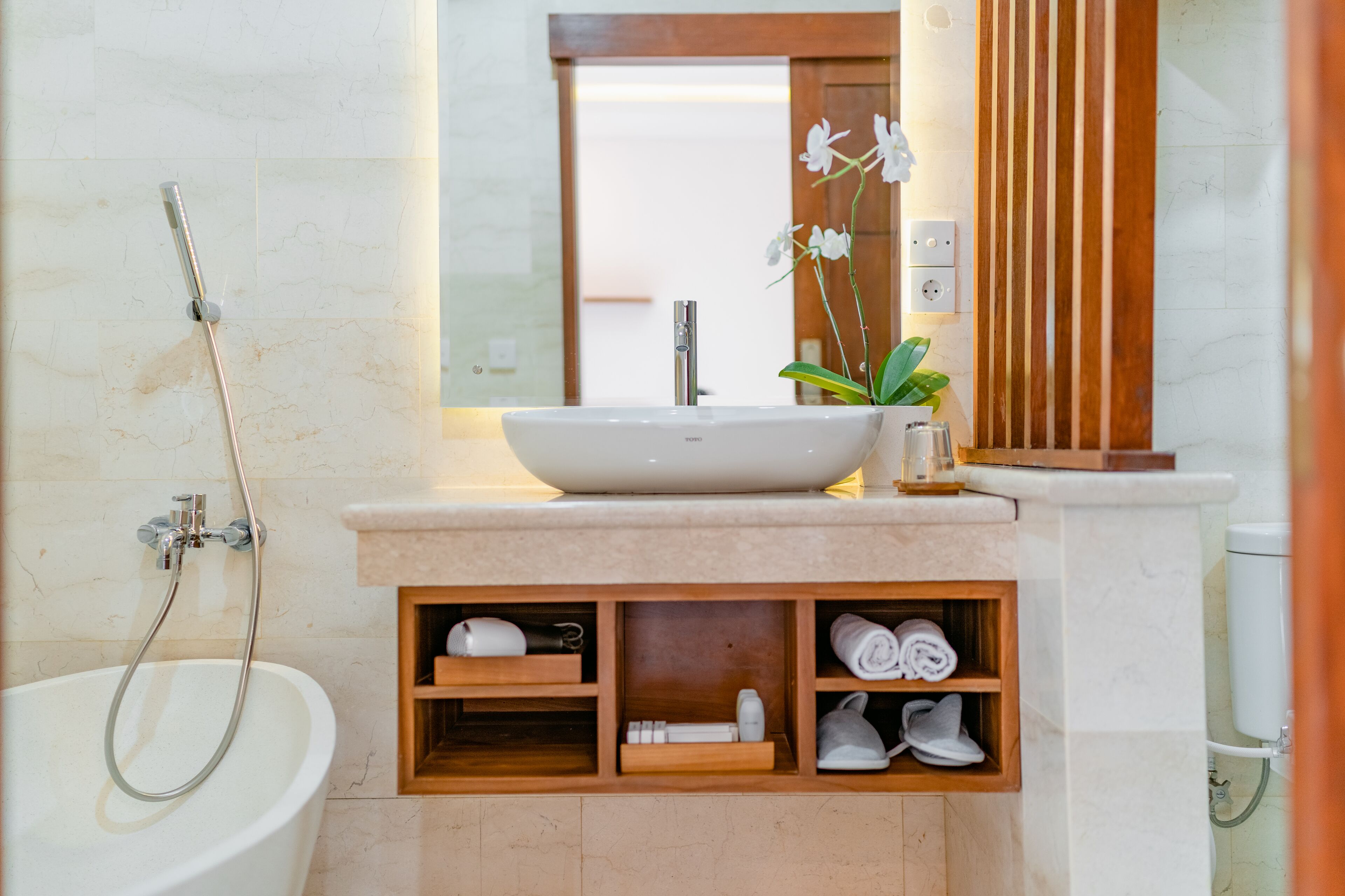 A bathroom with a bathtub, a sink, and a shower. There are wooden shelves with towels and toiletries.