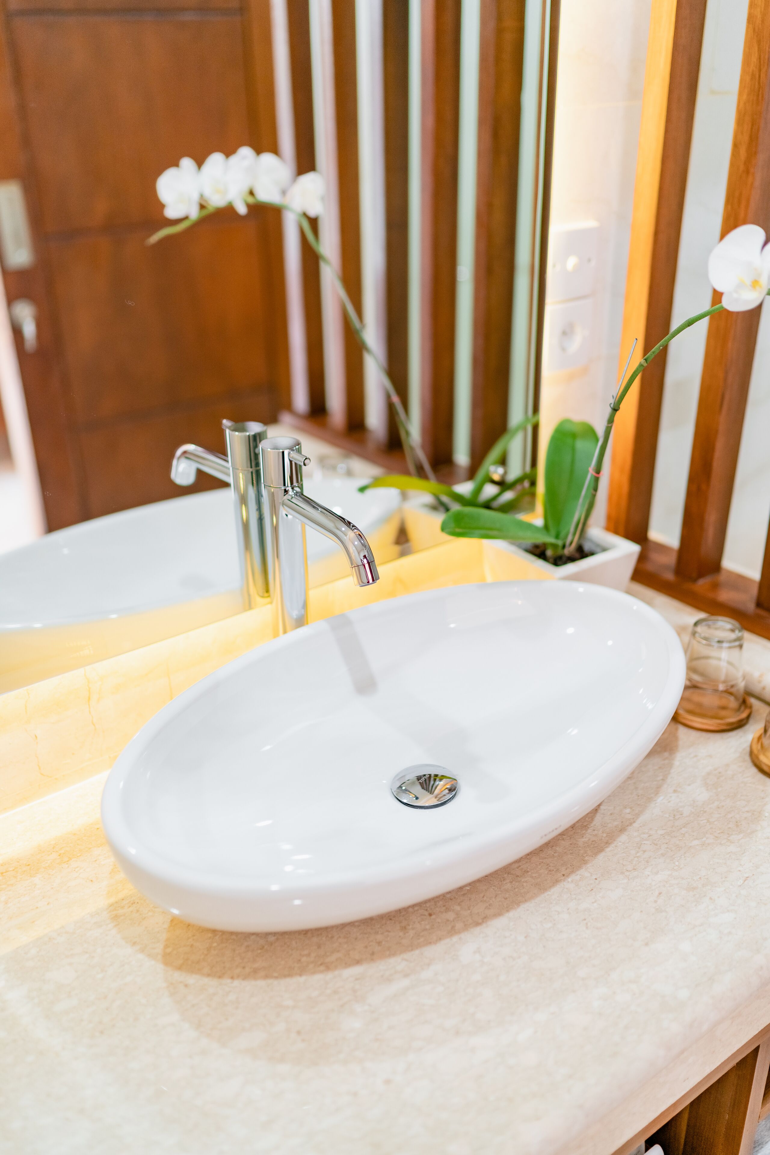 Une salle de bain avec un lavabo blanc, un miroir et une orchidée en pot.