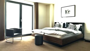 A modern bedroom with a large bed, a chair, a small ottoman, and a sliding glass door leading to a balcony. - Hotel im Wigbold Ochtrup (Ochtrup)