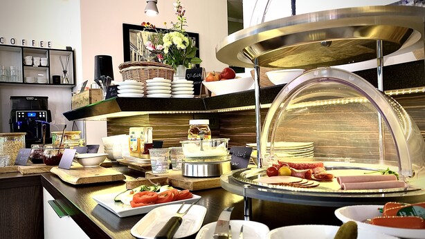 A buffet area with various food items, including fruits, cheeses, and meats, and a coffee station with cups and a coffee machine. - Hotel im Wigbold Ochtrup (Ochtrup)