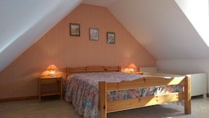 A bedroom with a sloped ceiling, wooden bed frame, floral bedspread, two bedside lamps, and two framed pictures on the wall. - Apartment 1: Apartment in private property with quiet courtyard (Bergheim)