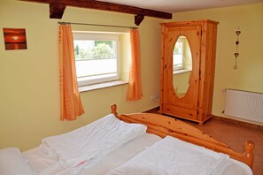 A bedroom with a wooden bed, a window with curtains, a wooden wardrobe, and a radiator.