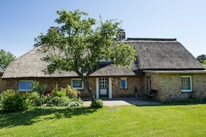 Ein traditionelles Backsteinhaus mit Strohdach, einer Haustür und einem kleinen Garten.