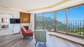 A spacious living area with a large window offering a mountain view, a flat-screen TV mounted on the wall, and a wooden cabinet.