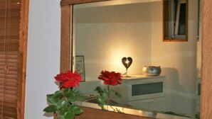 A room with a large mirror reflecting a desk, a lamp, and a small decorative item. There are two red flowers in a vase on the desk.