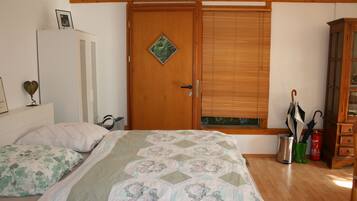 A bedroom with a wooden door, a bed with floral bedding, a bedside table, and a window with blinds.