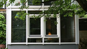A house with a grey exterior, a window with blinds, and a tree in front.