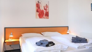Ett hotellrum med en säng, två kuddar, ett nattduksbord med en lampa och en tavla på väggen.