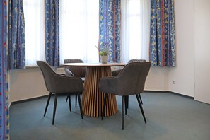 Kokoushuone, jossa on pyöreä puinen pöytä, neljä harmaata tuolia ja kuviolliset verhot.