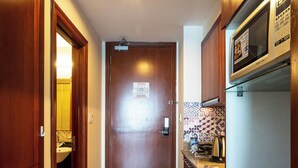 A narrow hallway with wooden doors, a tiled floor, a microwave, and a vending machine. - The Soulmate - Cozy studio central HCM  with  Rooftop Pool (Ho Chi Minh)
