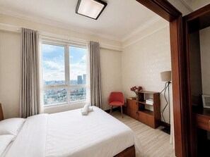 Habitación de hotel con una cama grande, un escritorio con lámpara, una silla y vistas a la ciudad a través de la ventana.