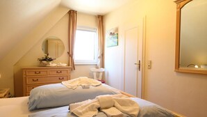 A bedroom with two beds, a dresser, a mirror, and a window with curtains.