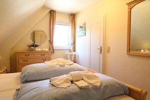 A bedroom with two beds, a dresser, a mirror, and a window with curtains.