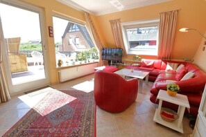 A living room with a red sofa, a television, and a view of a building outside.