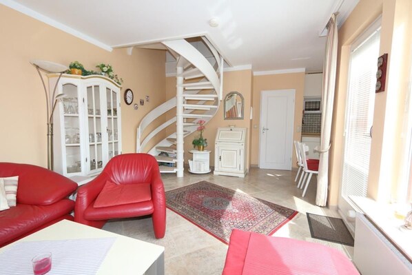 Un salon avec un canapé en cuir rouge, un meuble blanc, un escalier en colimaçon et un coin repas avec des chaises.