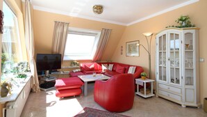 A living room with a red sofa, a television, a cabinet with glass doors, and a window with curtains.
