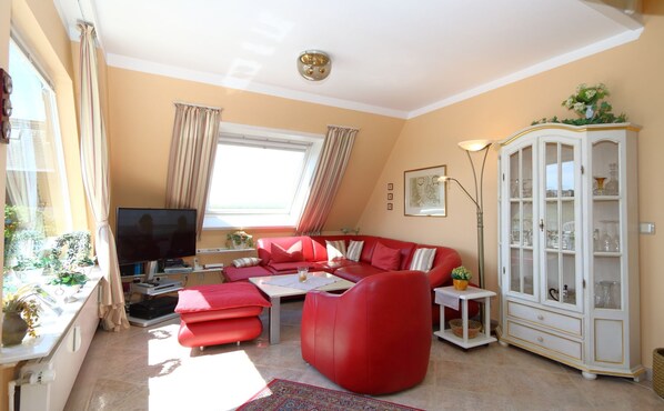 A living room with a red sofa, a television, a cabinet with glass doors, and a window with curtains.