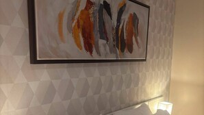 Een hotelkamer met een wand met een geometrisch patroon, een ingelijst abstract schilderij en een netjes opgemaakt bed met witte lakens.