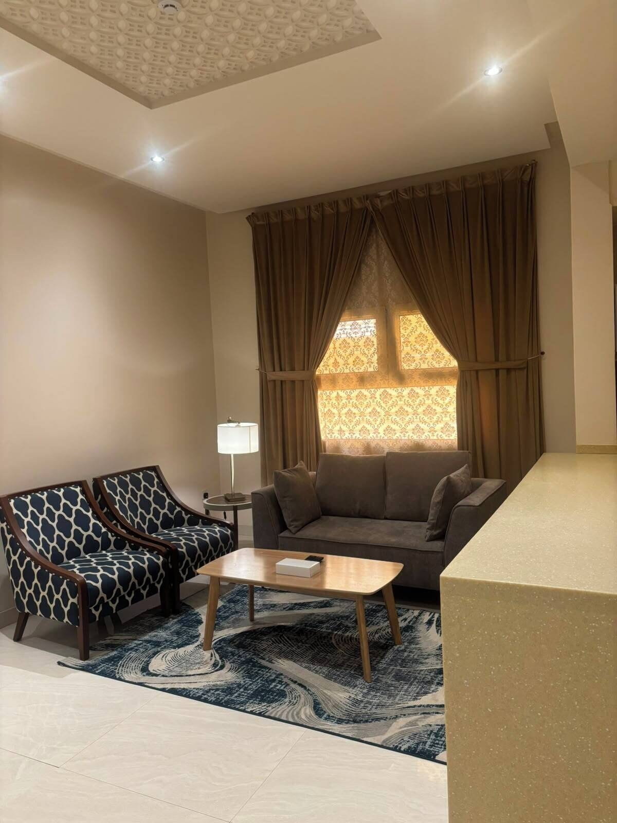 A living room with a sofa, two armchairs, a coffee table, and a patterned rug.