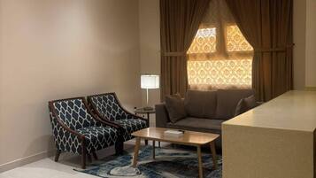 A modern living room with a sofa, a patterned armchair, a coffee table, and a large window with curtains.
