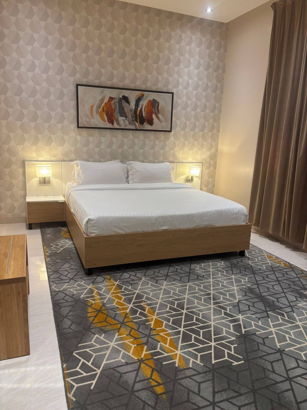 A modern hotel room with a large bed, geometric patterned carpet, and a geometric wall design.