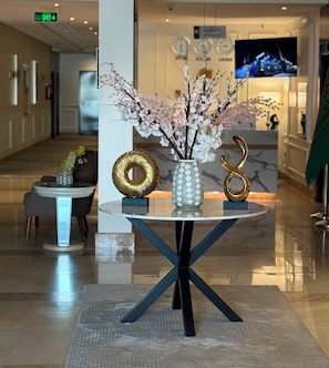Un vestíbul amb una taula rodona que presenta un vas amb flors, dos objectes daurats decoratius i un disseny modern.