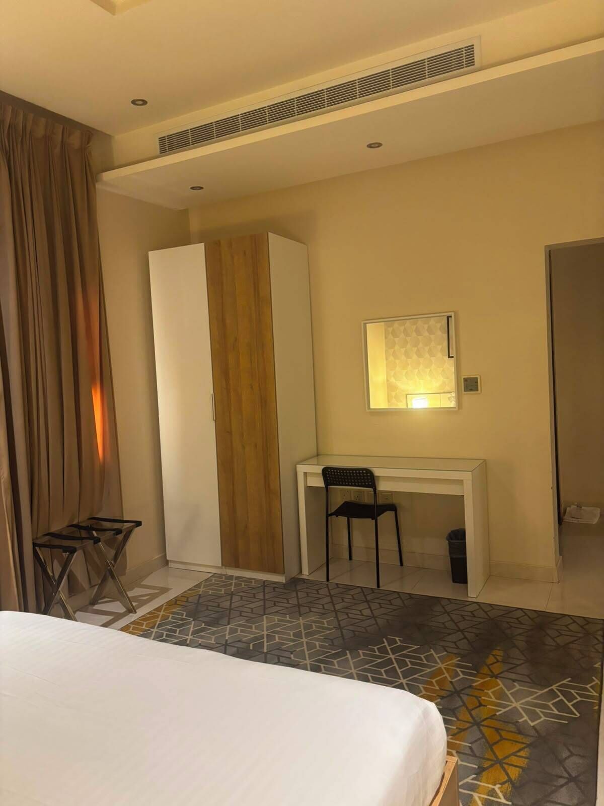 A hotel room with a bed, a desk, a chair, a wardrobe, and a mirror.