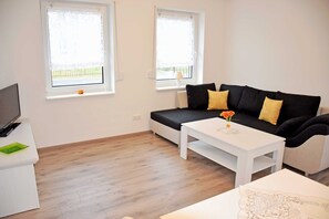 A modern living room with a black sofa, white coffee table, and a TV on a white stand.