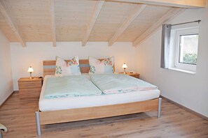 A bedroom with a wooden ceiling, a bed with two pillows, a nightstand with a lamp, and a window.