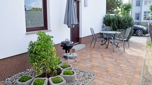 Een terras met een barbecue, buitenmeubels en plantenbakken.