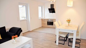 Een moderne woonkamer met een witte bank, een eettafel met stoelen, en een keuken op de achtergrond.