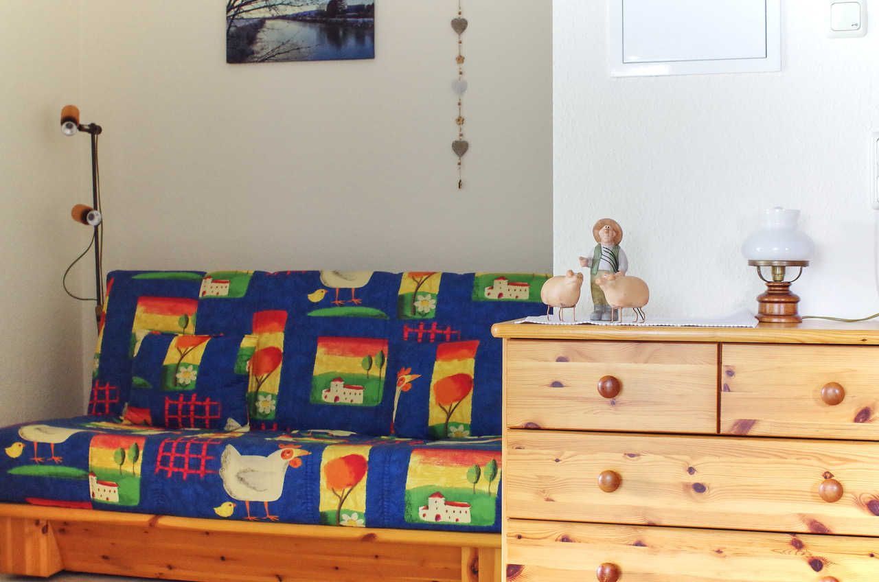 Una habitación con un sofá colorido, cómoda de madera y adornos en la pared, incluyendo un cuadro y un adorno colgante.