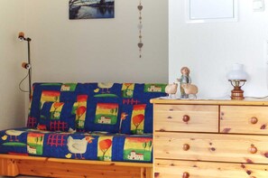 A room with a colorful sofa, wooden dresser, and wall decorations including a painting and a hanging ornament.
